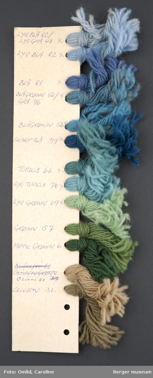 Pappremse med hull på en side, der garnprøver i forskjellige farger er knyttet på. Garnfargene er nummerert med blå kulepenn på kartongen.