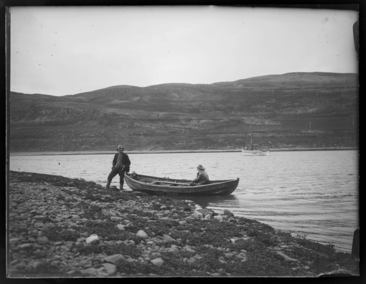To menn og en liten gutt med robåt i fjæra. Gutten og den ene mannen sitter i båten, mens den siste står ved rekka på båten som er trukket delvis på land. Ute på fjorden er det en skøyte. Sommer