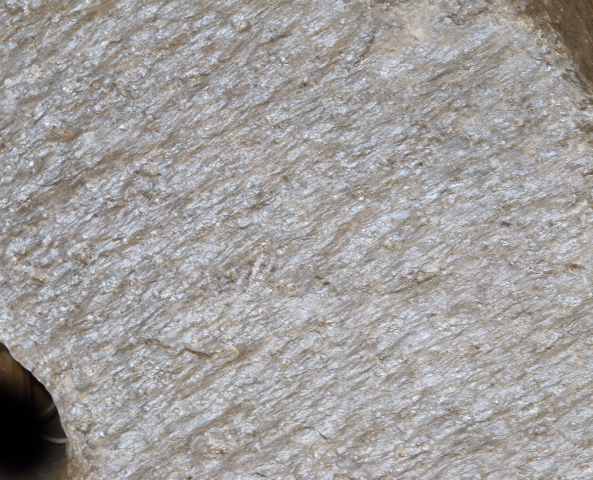 En kvernstein, riflet regelmessig overflate. Sirkelrundt hull, plassert midt i steinen.