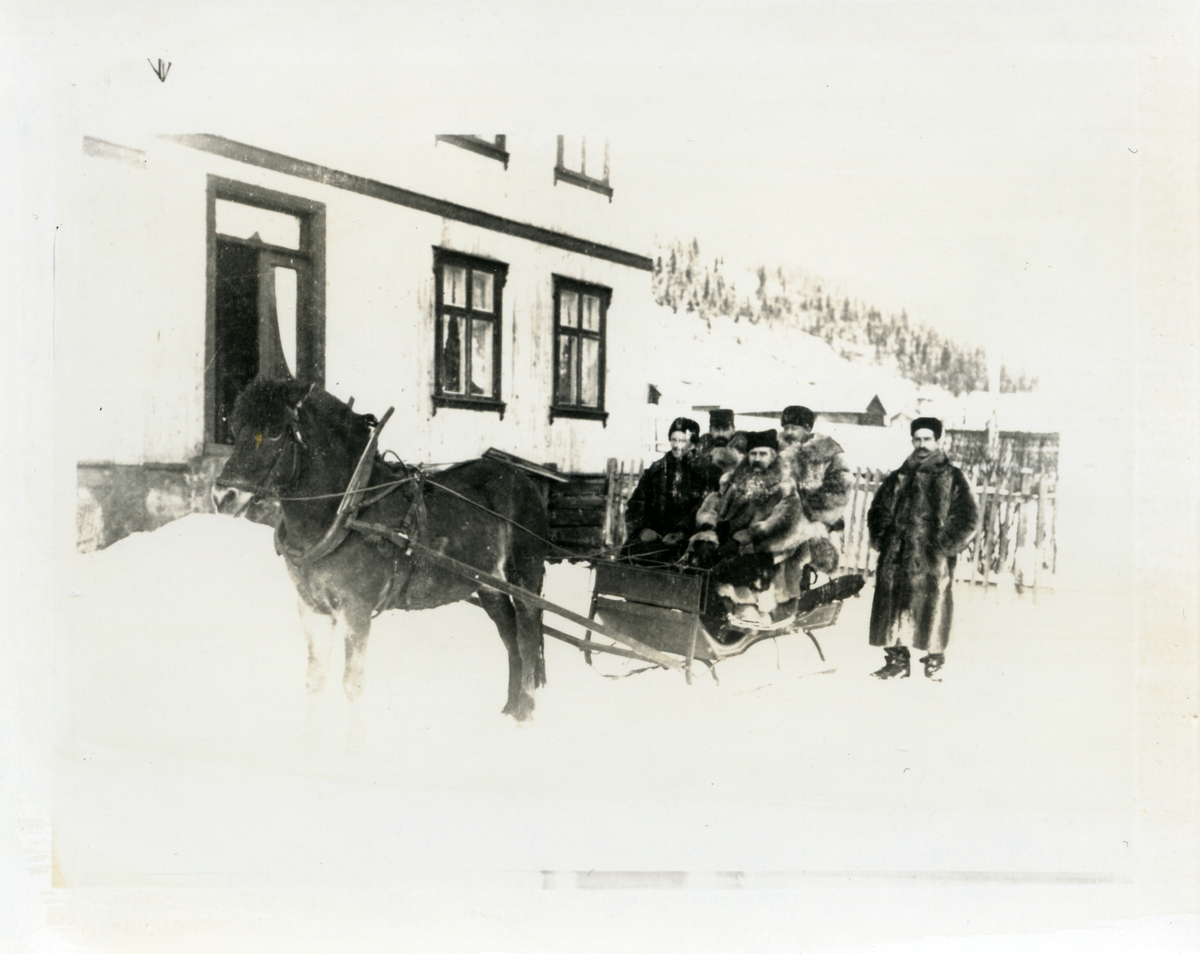 4 pelskledde menn sitter på en slede med hest foran. Bildet er tatt utenfor bygningen på Onstadmarken, Nord-Aurdal. Vinter og snø. Tatt mellom 1890 og 1895