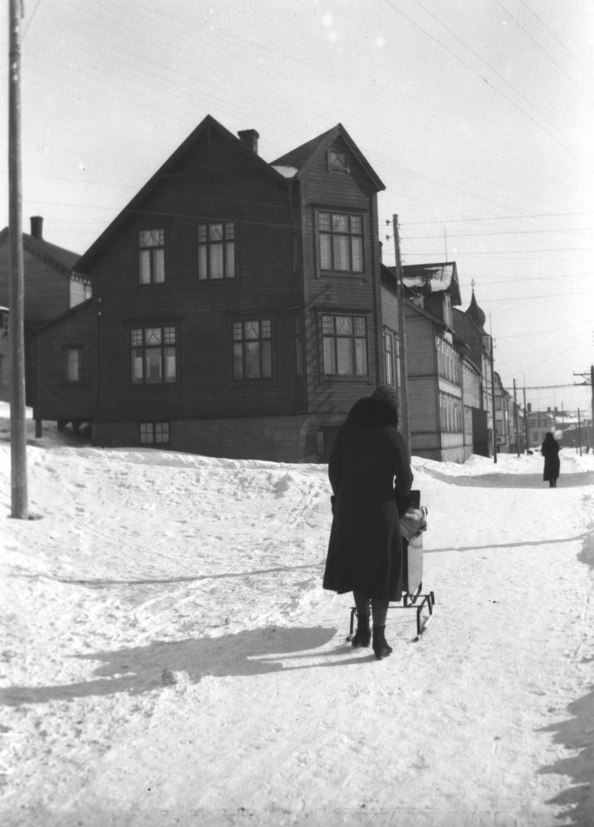 En dame går bortover Havnegata med barnevogn en vinterdag. Sellstrømgården er den nærmeste bygningen.