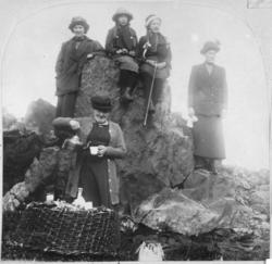 Damer og jenter som sitter og står på en stor stein. Foran s