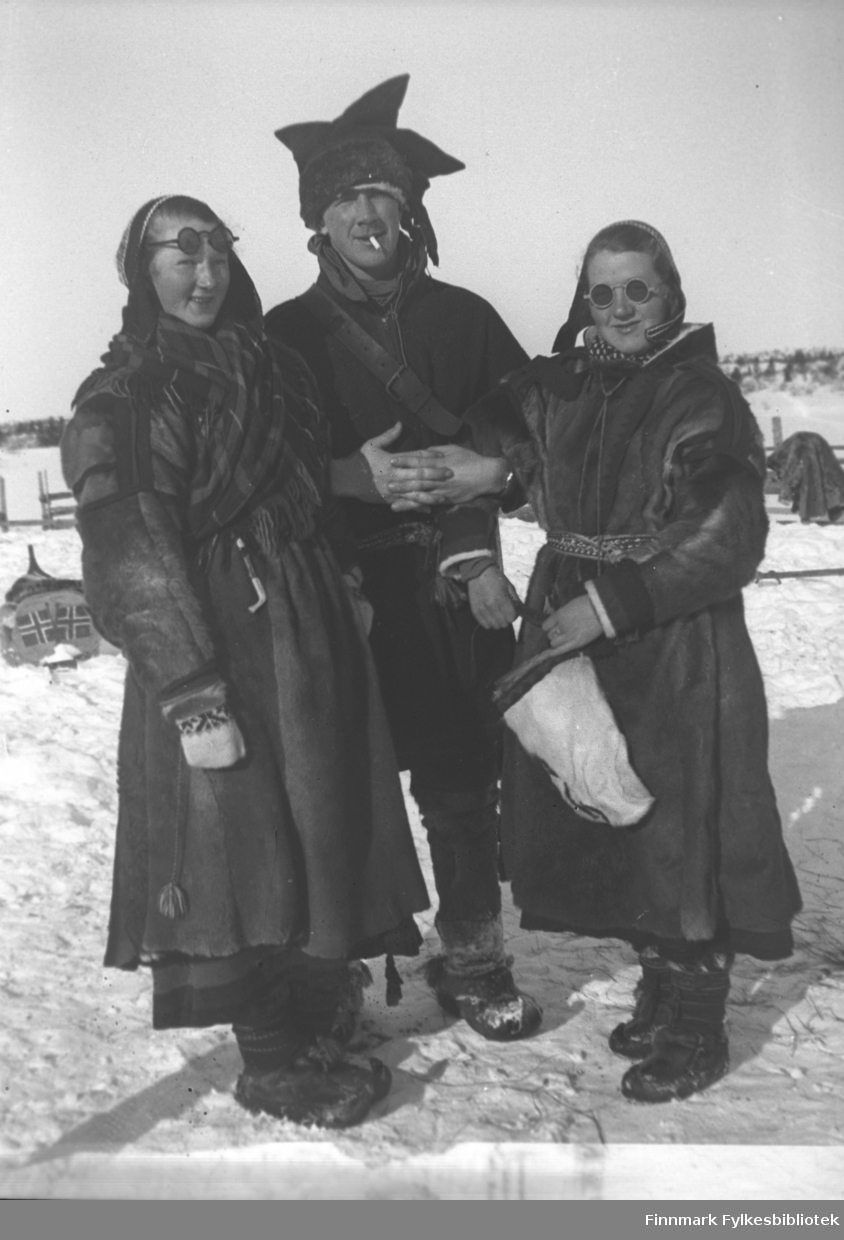 Pakanajoki i 1936. Fra venstre Marine Mikkola, Per Sivle Olsen og Synnøve Mikkola, alle kledt i samiske klær, pesker og kofter. I bakgrunnen en pulk, påmalt norske flagg på akterspeilet. 