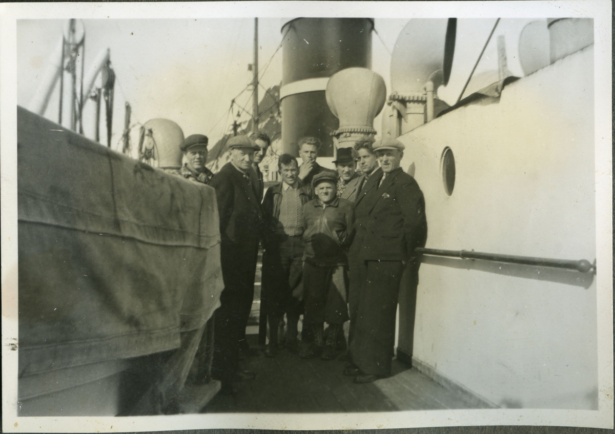 Flere ukjente menn ombord på en båt som muligens kan være hurtigruten. Bildet er kanskje tatt før eller under krigen, på 40-tallet. Mennene er kledd i jakker, strikkede gensere, bukser, hatter og luer.