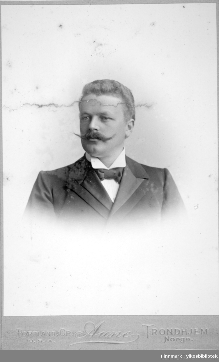 Portrett av en mann med mørk dressjakke, hvit skjorte med høy krage og sløyfe i halsen.