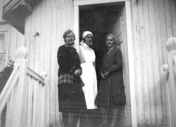 Tre damer står i inngangspartiet/vindfanget til et hus. Døre