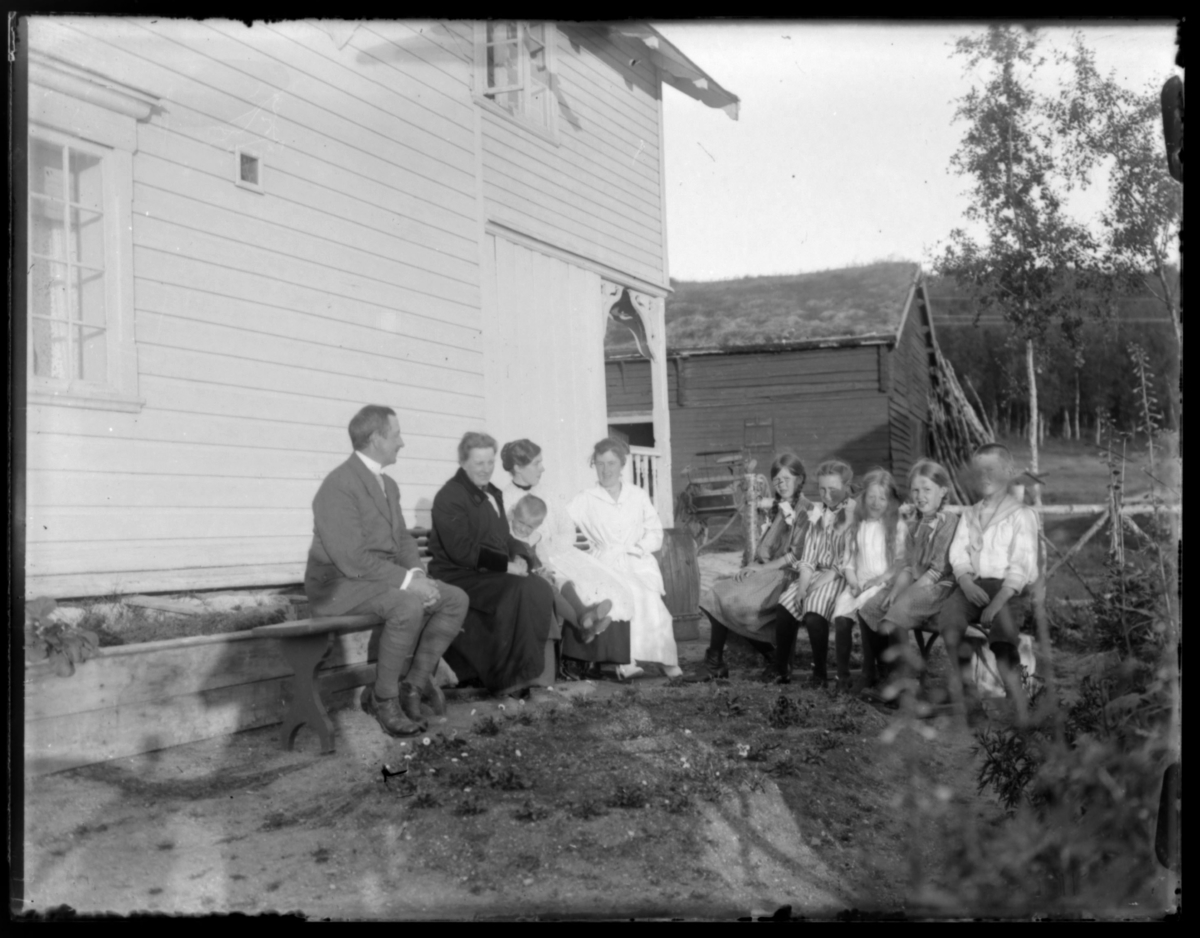 Gruppebilde av barn og voksne på gården Strømsnes i Jarfjord, eid av lensmann Thoralf Bertelsen (mannen til venstre). Damen som sitter høyre side av bildet er Thoralf sin kone Aagot Bertelsen (f. Esbensen). Gutten (i matrosdress) på høyre side av bildet er Einar Bertelsen. Litt usikkert hvem er de andre barna, men mest sannsynlig at to av dem er Elsa Bertelsen (f. 1906) og Aagot Bertelsen (f. 1909). Fru Grasmo (Anne Marie) er nr. to fra venstre. Samme motiv som i Fb.83002-423