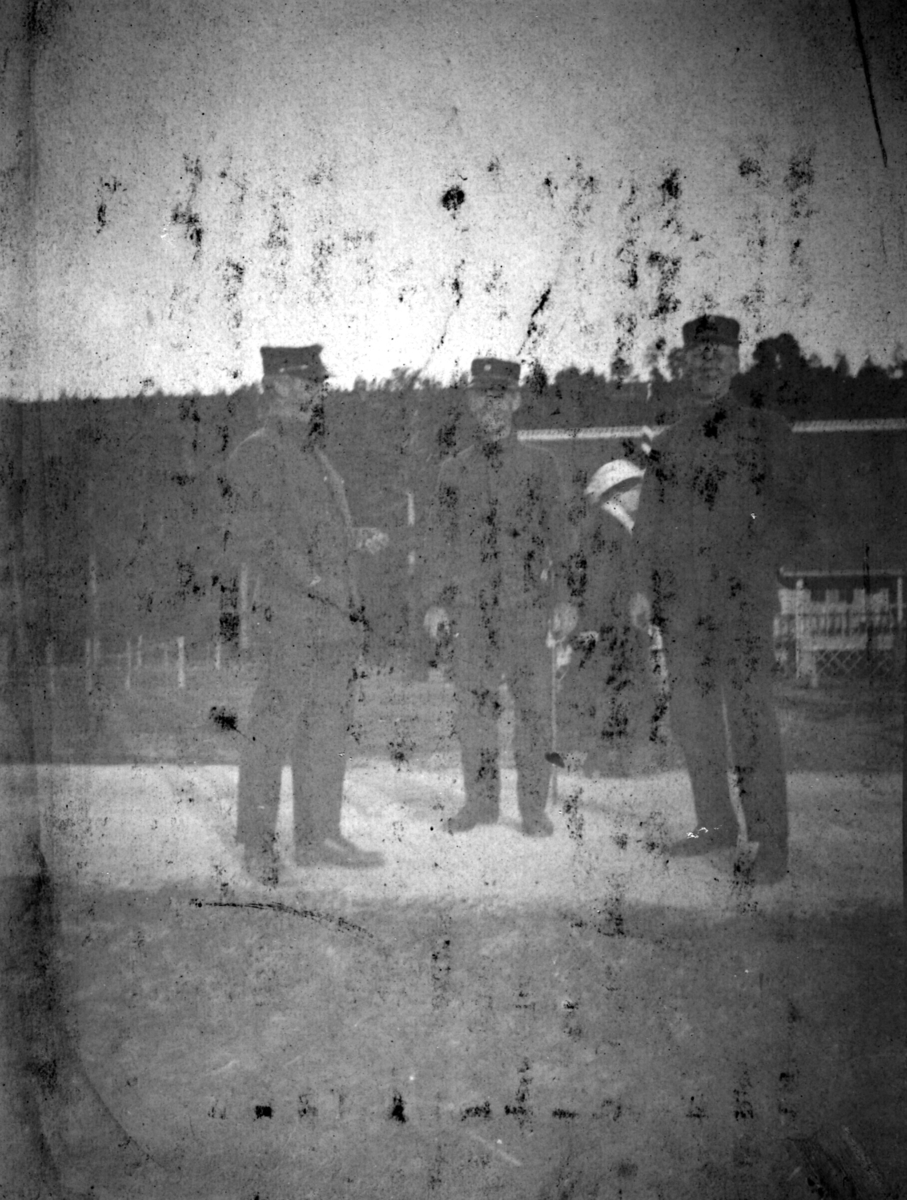 "Fra Altengård". Bildet tattt i Altagård. Tre menn i uniform står på en vei. Bak mennene kan man se en kvinne, gjerde og skog.