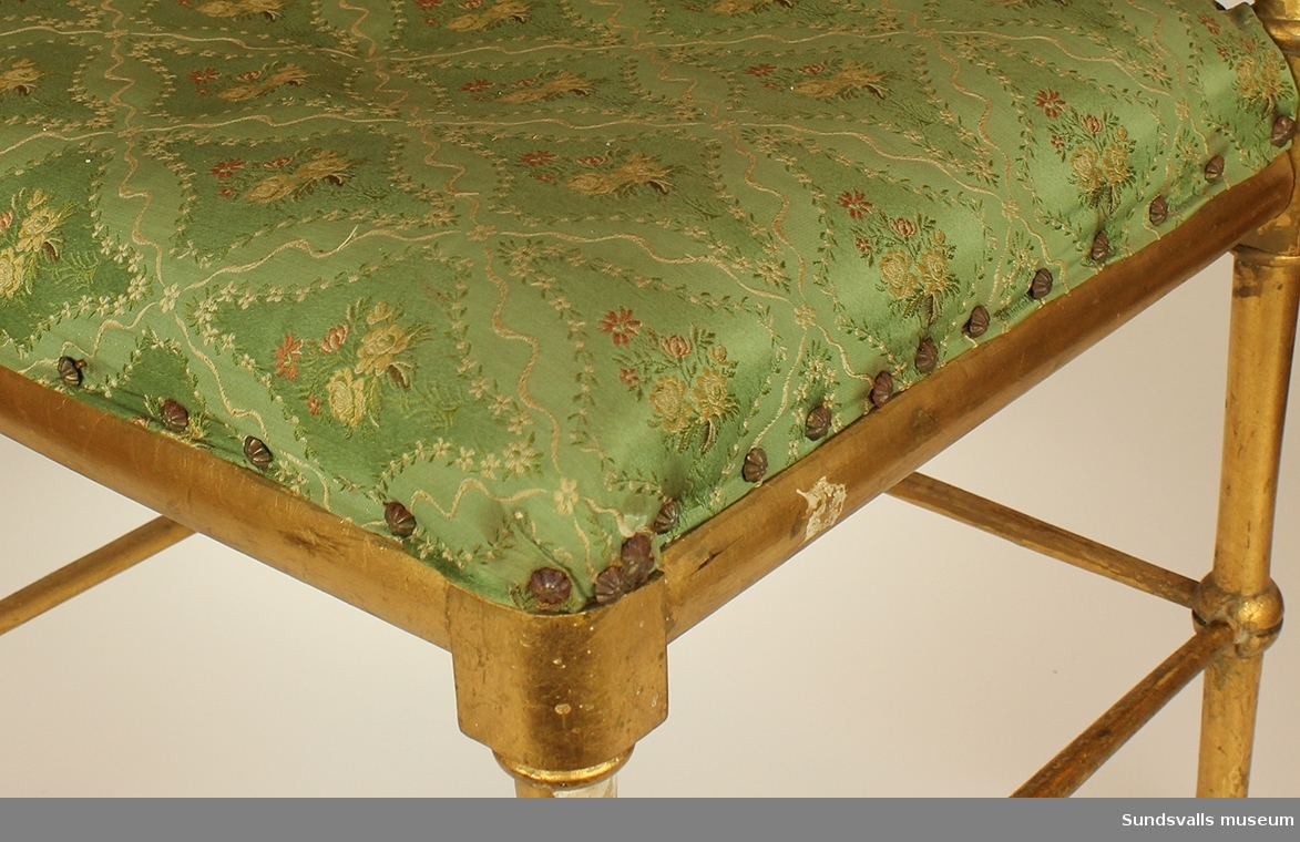 En guldkolorerad svarvad björkstol. Sits av sadelgjord och tagelfylld dyna som klätts med vit och rödblommigt grönt möbeltyg vilket fastsatts med möbelspik i form av stiliserade prästkragar. Nr 2 av ett par.