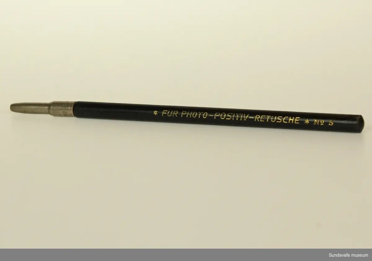 Svart penna med stifthållare av metall och träkropp som ska fyllas med ritstift för retuscheringsarbeten.