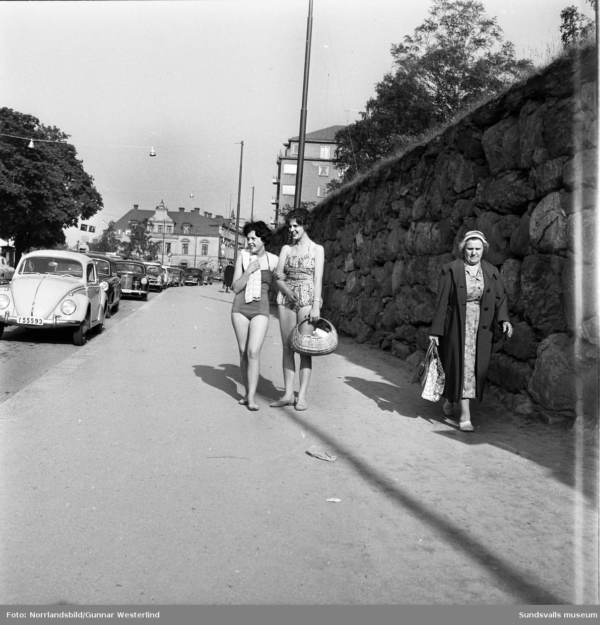 Två unga kvinnor med baddräkt och picknickkorg vid Bünsowska tjärnen och promenerande på Storgatan, nedanför kyrkan.