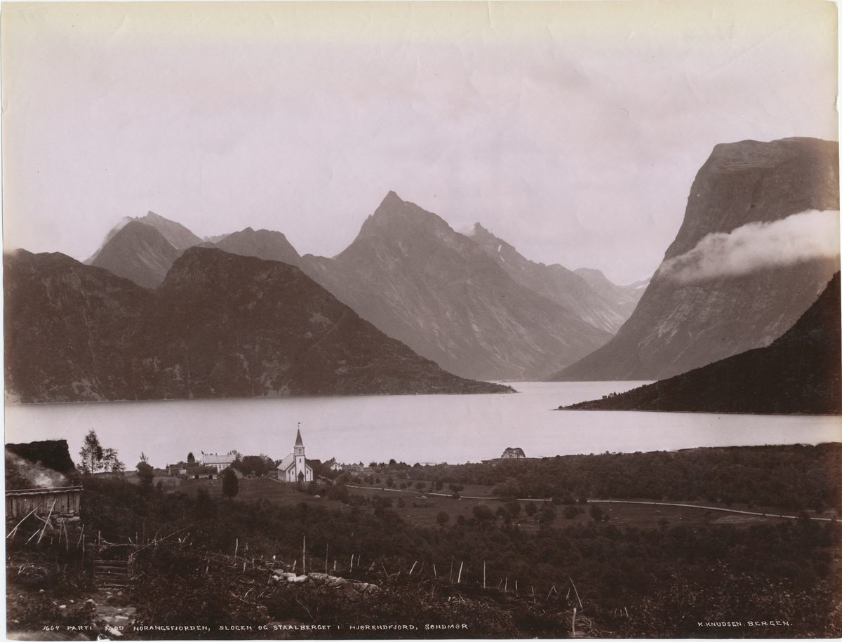 Utsikt mot Norangfjorden, Slogen og Stålberget i Hjørundfjord. Kirke og andre hus i forgrunnen.