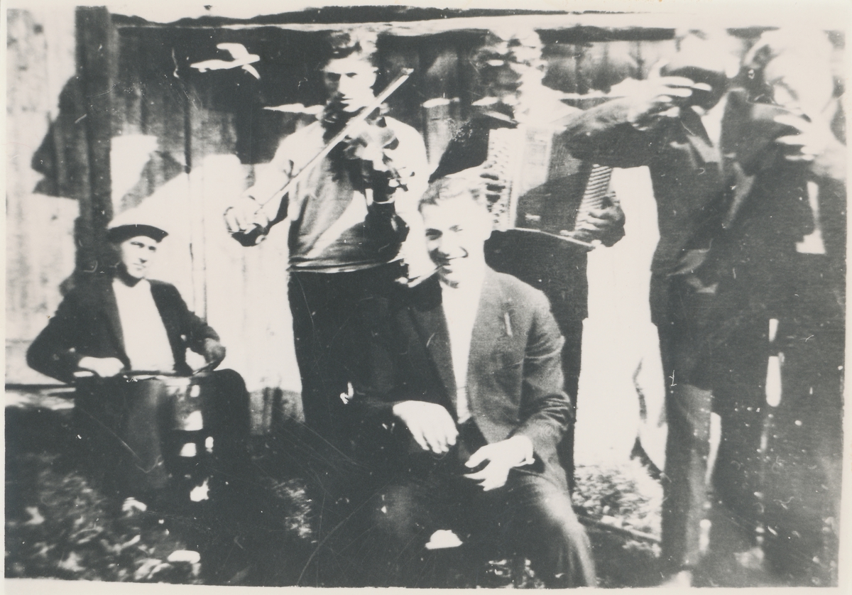 Motiv av seks menn, et spelemannslag og to herrer som drikker av en skål. Avslutning av slåttedugnad på Skotet ca.1928-30.