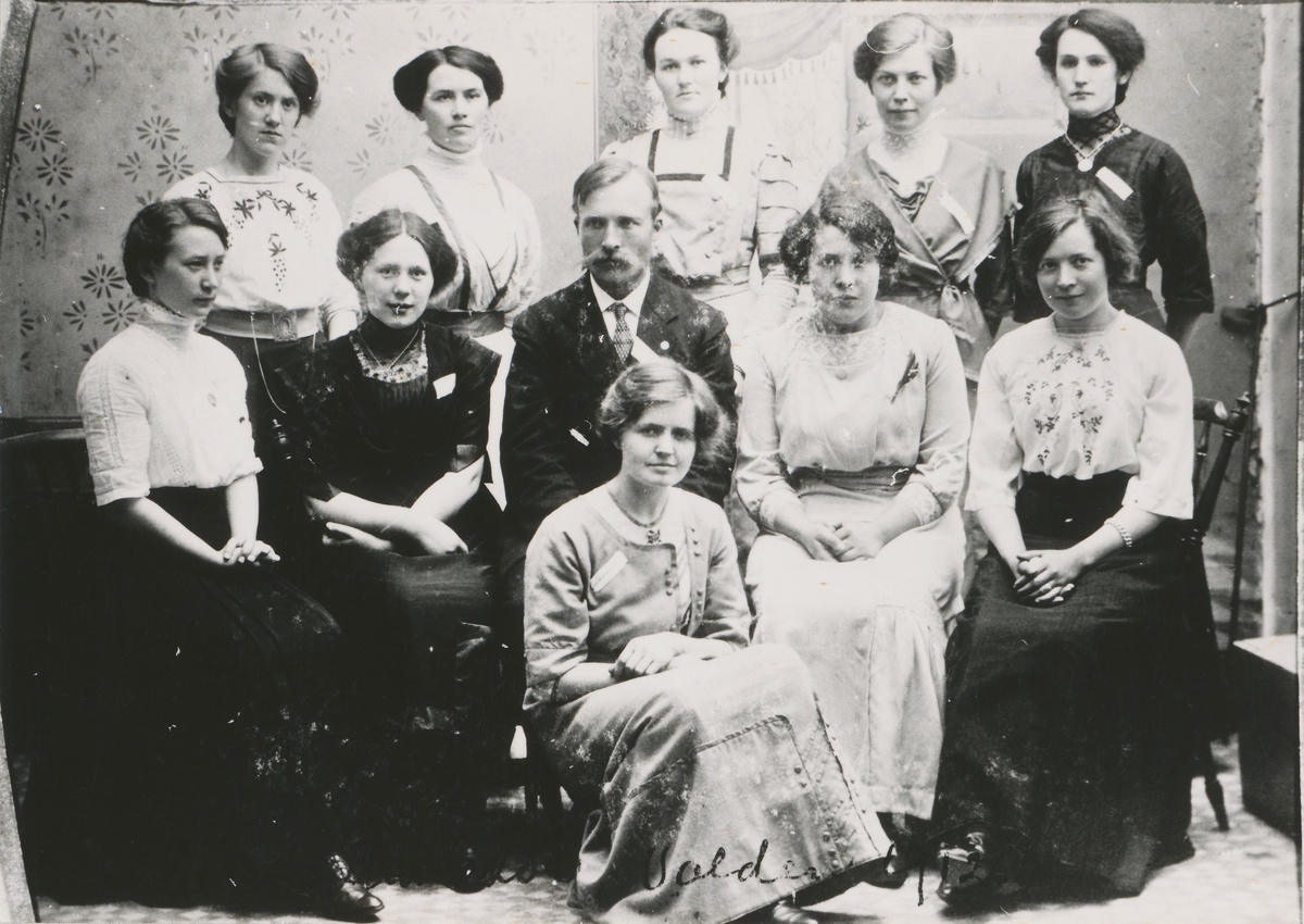 Gruppefotografi av solistkoret Volda, 1915. Dirigenten, Peder Eiken, i midten og ti kvinner.