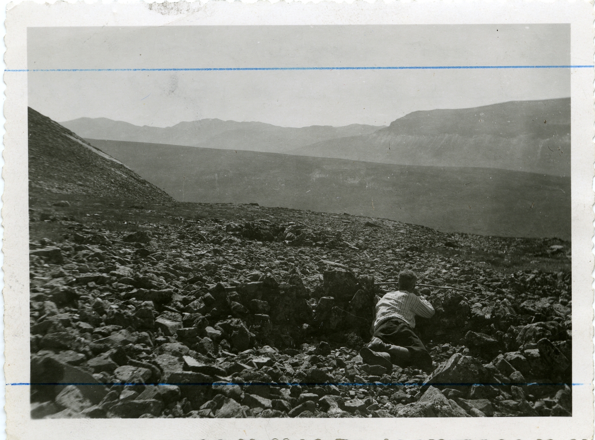 Mann liggende bak en "Steinmur", i et "bøgahi." Bildet er fra Vang i Valdres.