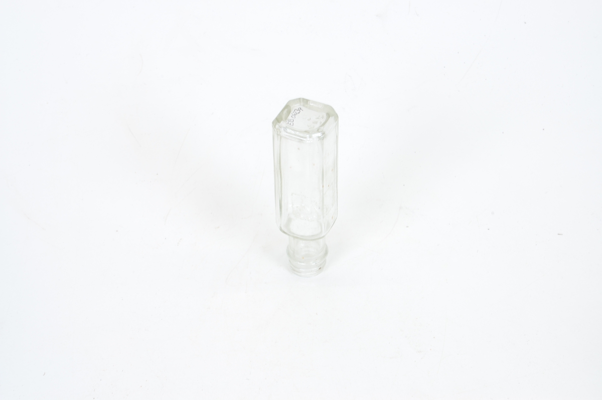 Form: firkantet flaske med avkuttede hjørner. Liten og synn, rund tut, mangler kork, men har gjenger til kork
