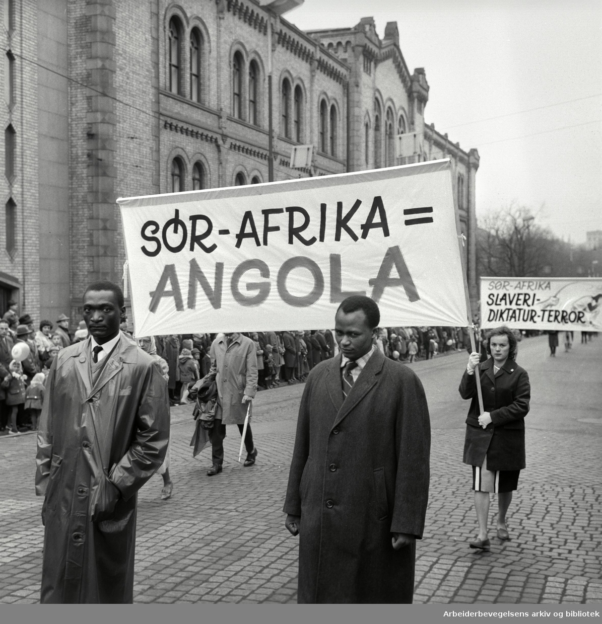 1. mai 1963 i Oslo.Demonstrasjonstoget i Karl Johans gate..Parole: Sør-Afrika = Angola.Parole: Sør-Afrika.Slaveri - Diktatur - Terror