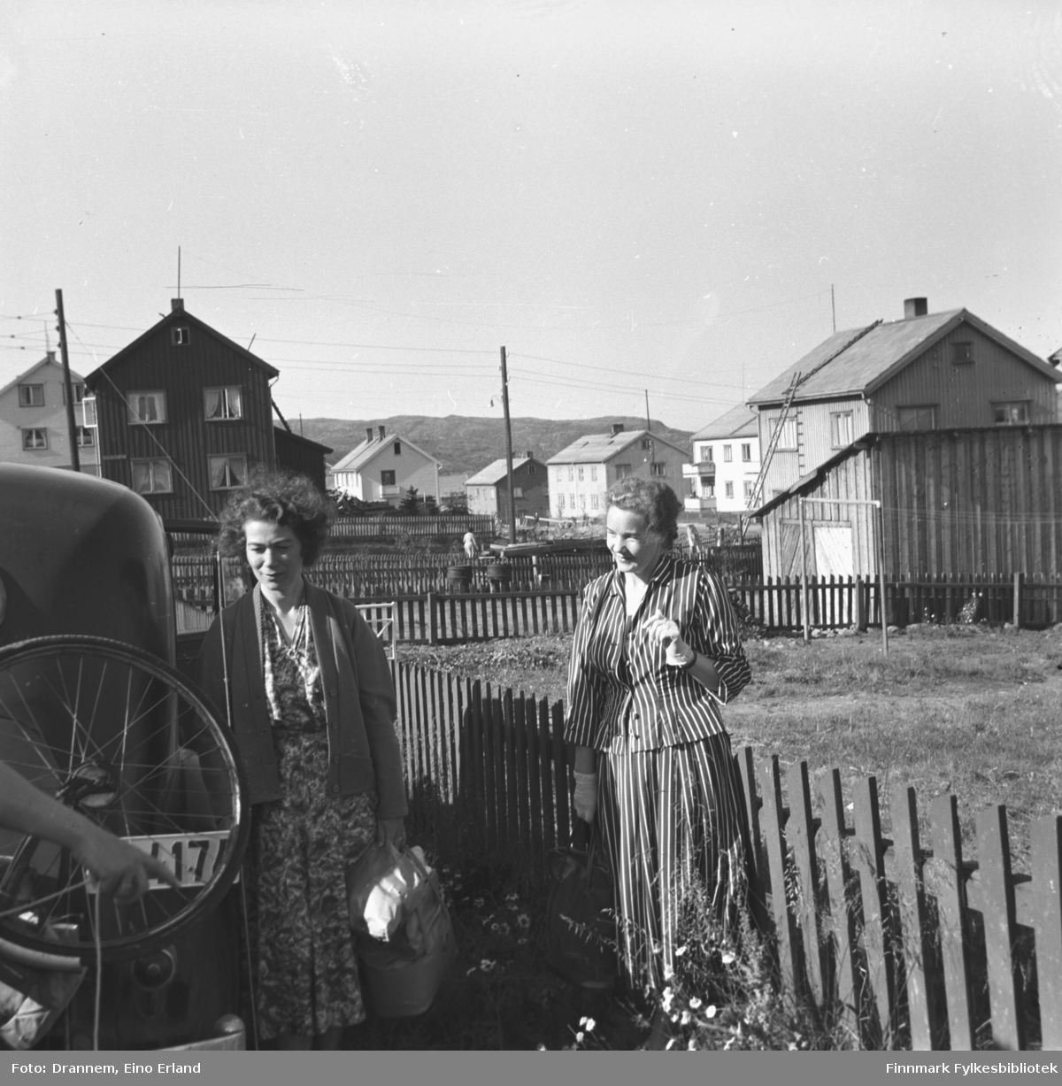 Jenny Drannem og Synnøve Vorren fotografert ved en bil. Begge har en veske i hånda. Man ser i bakgrunnen gjenreisningshus. Stedet er Kirkenes