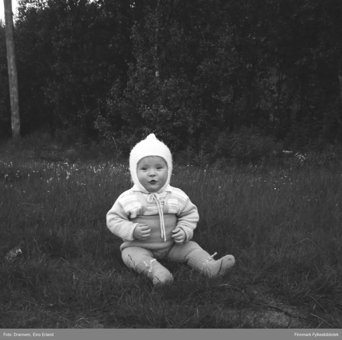 Bilde av et litet barn, antakelig Karl Magne Arvola, som sitter i gresset. Bildet er tatt sannsynligvis i Neiden.