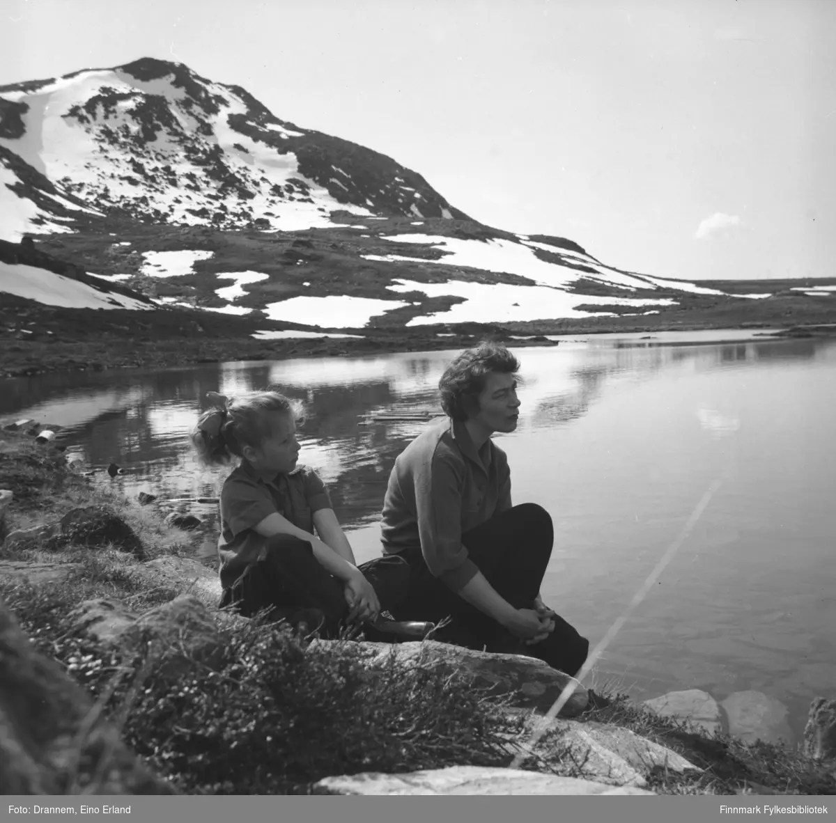Portrett av mor og datter, Jenny Drannem og Turid Lillian sitter ved innsjøen. Det er fortsatt noen snøflekker her og der i fjellet