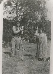 Ei kvinne og en mann driver slåttonn. Kvinna har ei rive i h