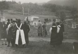 En gruppe mennesker står å ser mot en buss på veien lenger b