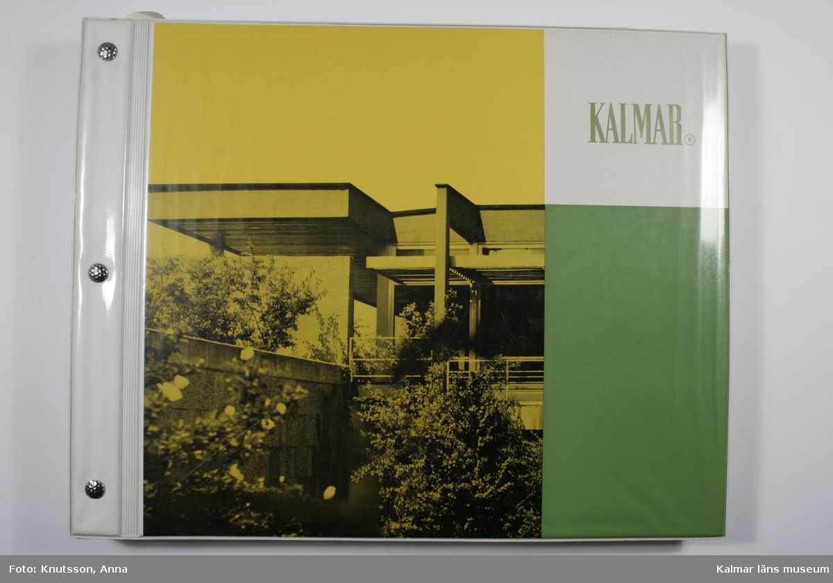KLM 33295. Tapetkatalog. Vit, gul och grön pärm i plast med fotografi av en byggnad. Tapetkatalog för Kalmar Nya Tapetfabrik, innehåller många olika prover av tapeter från 1970-talet.