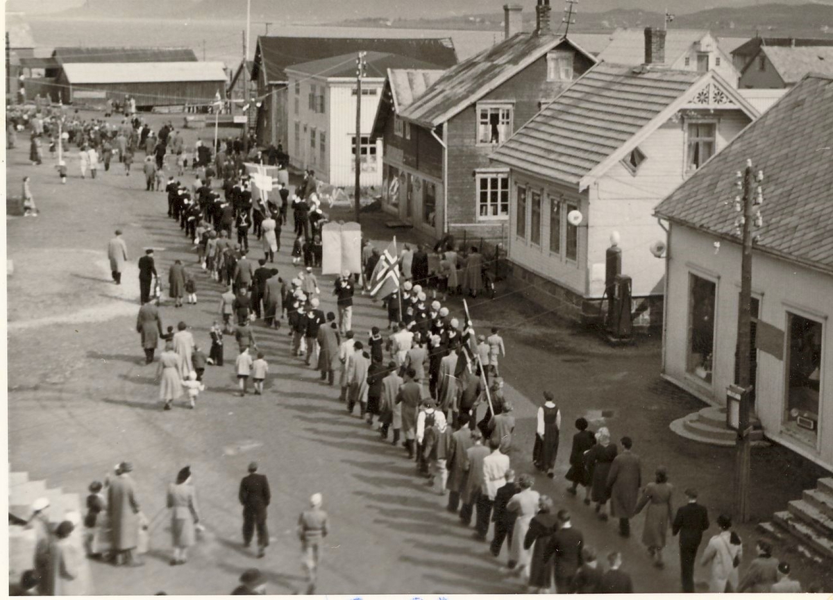 17. mai-tog i Strandgata på Sortland 1950. Fra venstre: Rødhuset, slakteriet, Pedersen sykkelverksted, Steiro m/bensinpumpa, Lührs elektriske forretning