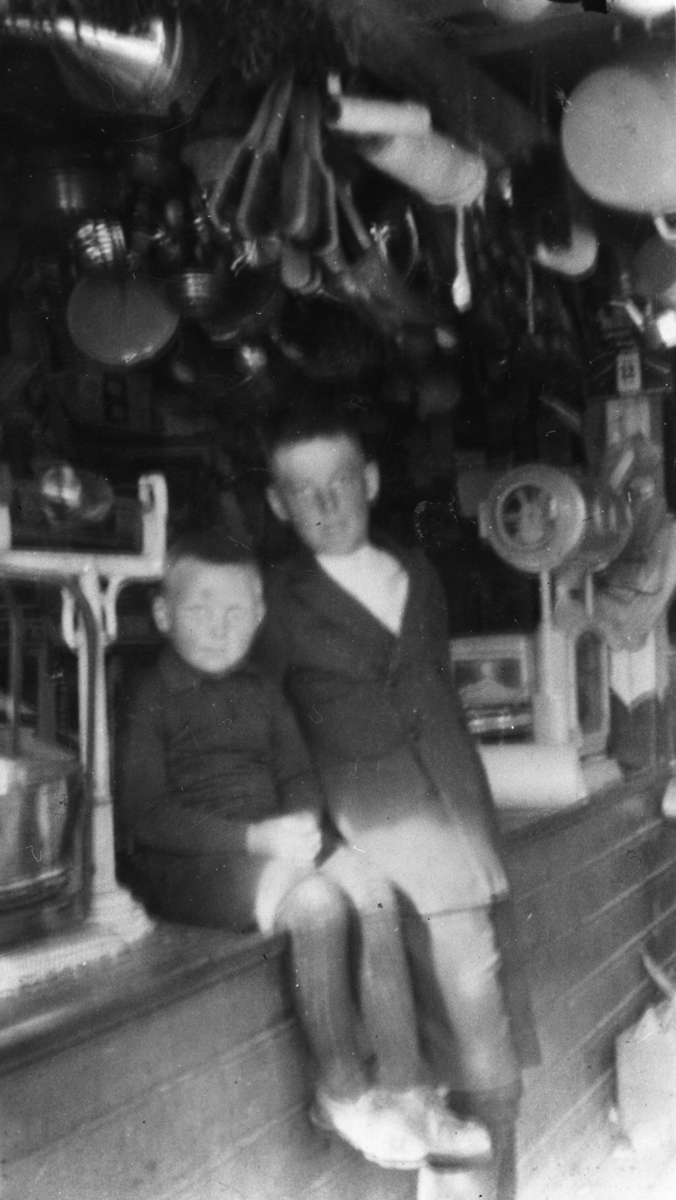 Bildet er tatt fra forretningen til Gaare, ca 1916-17. Fra venstre Bjarne Jørstad og Arnold Rolfsen. Forretningen var i kjelleren til Odin Kvello. Guttene sitter på disken ved siden av en vekt. I taket henger det forskjellig utstyr.