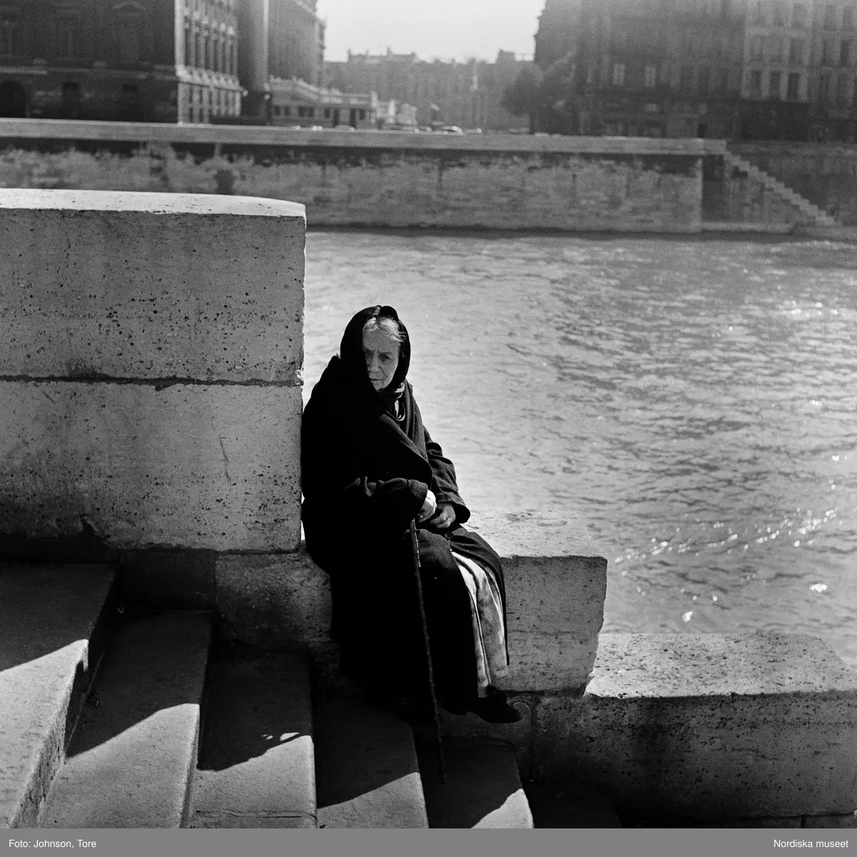 Paris. En äldre kvinna sitter på kajkanten vid Seine.