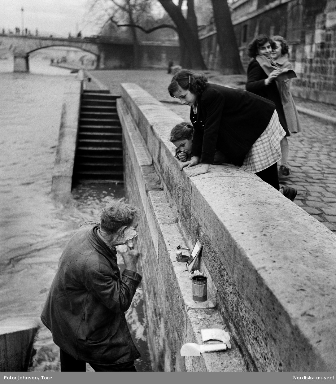 Paris. En man rakar sig vid kajen längs Seine iakttagen av några flickor.