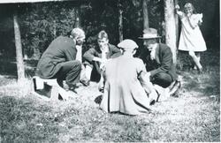 Fire menn sitter og spiller kort i skogen iført søndagsantre