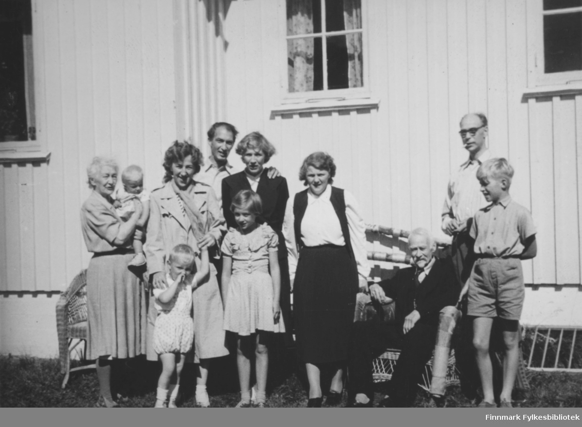 (Samme bilde som FBib.08039-016) Familiene Sælø og Noodt hos Hanna og Eilert Noodt i Langnes i Tana i 1954.  Fra venstre: Hanna Noodt med lille Marianne Noodt på armen, Elsa Sælø med Jan Erik Sælø i handa,  Håkon og Solveig Noodt (bak), Kari Noodt (foran Solveig),  Mossik Noodt, Eilert Noodt sitter på stolen, Leif Noodt og Terje Noodt. Ivar Sælø har tatt bildet.