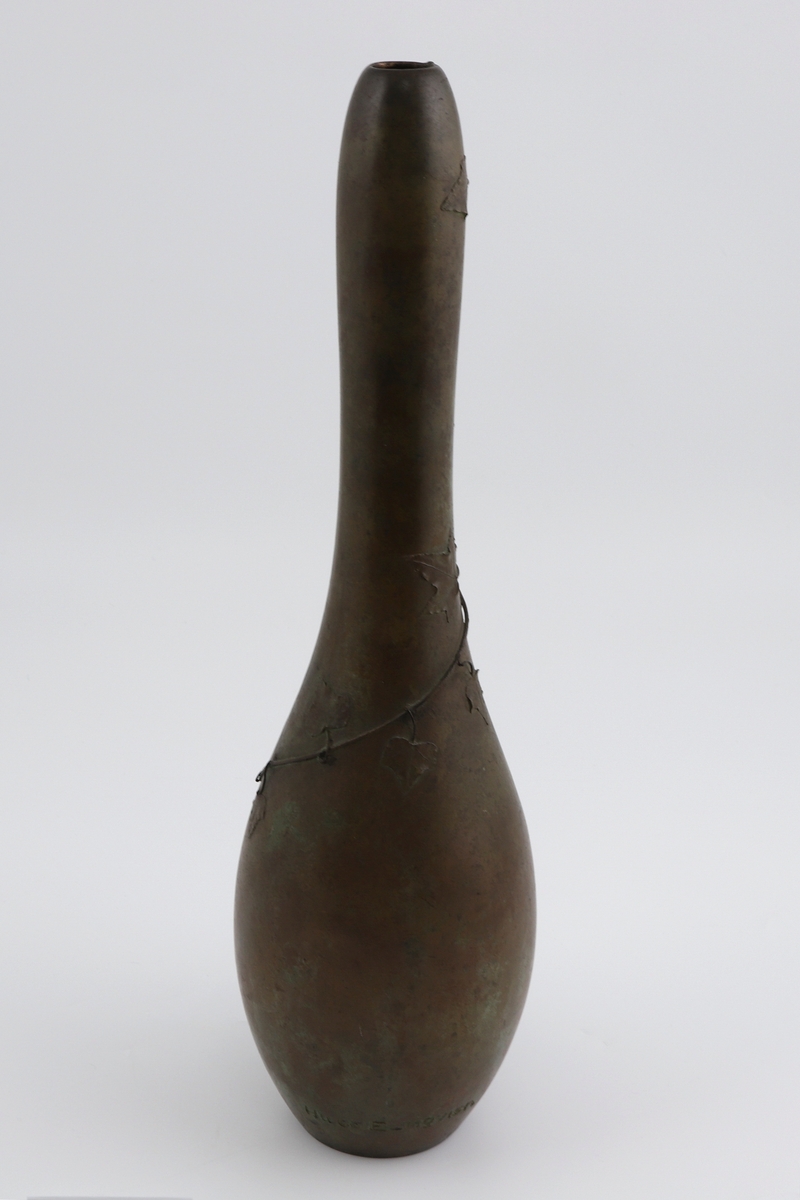 Høyreist pæreformet vase i støpt bronse. Ovalformet korpus som glir over i en meget langstrakt hals. Rundt halsen og på øvre del av korpus er det fremstilt en slyngende eføygren i lavt relieff, samt en plastisk utformet bille.