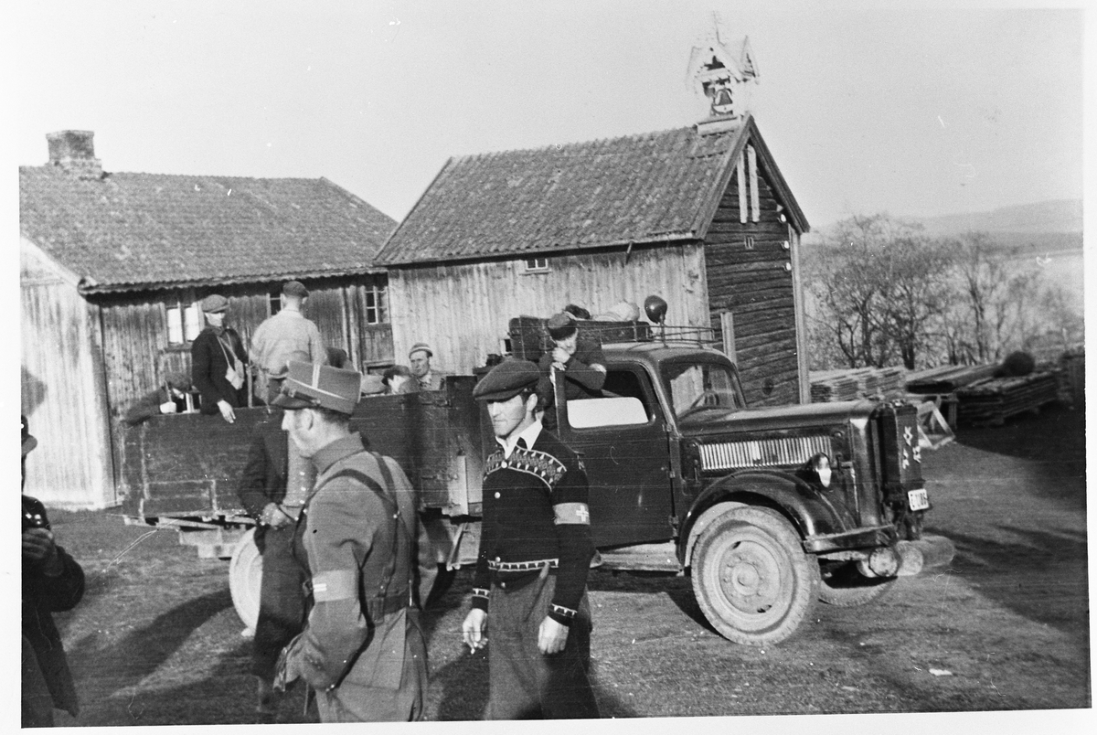 Milorg-karer på Fjeldhaug søndre, Totenvika, i maidagene 1945. Foran står Finn Gjestvang og Emil Oppegård. Oppi lastebilen står Leif Hørland. I førerhuset sitter John Taralrud.