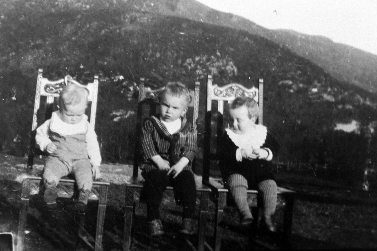 Amatørportrett av tre små gutter som sitter på hver sin stol utendørs.