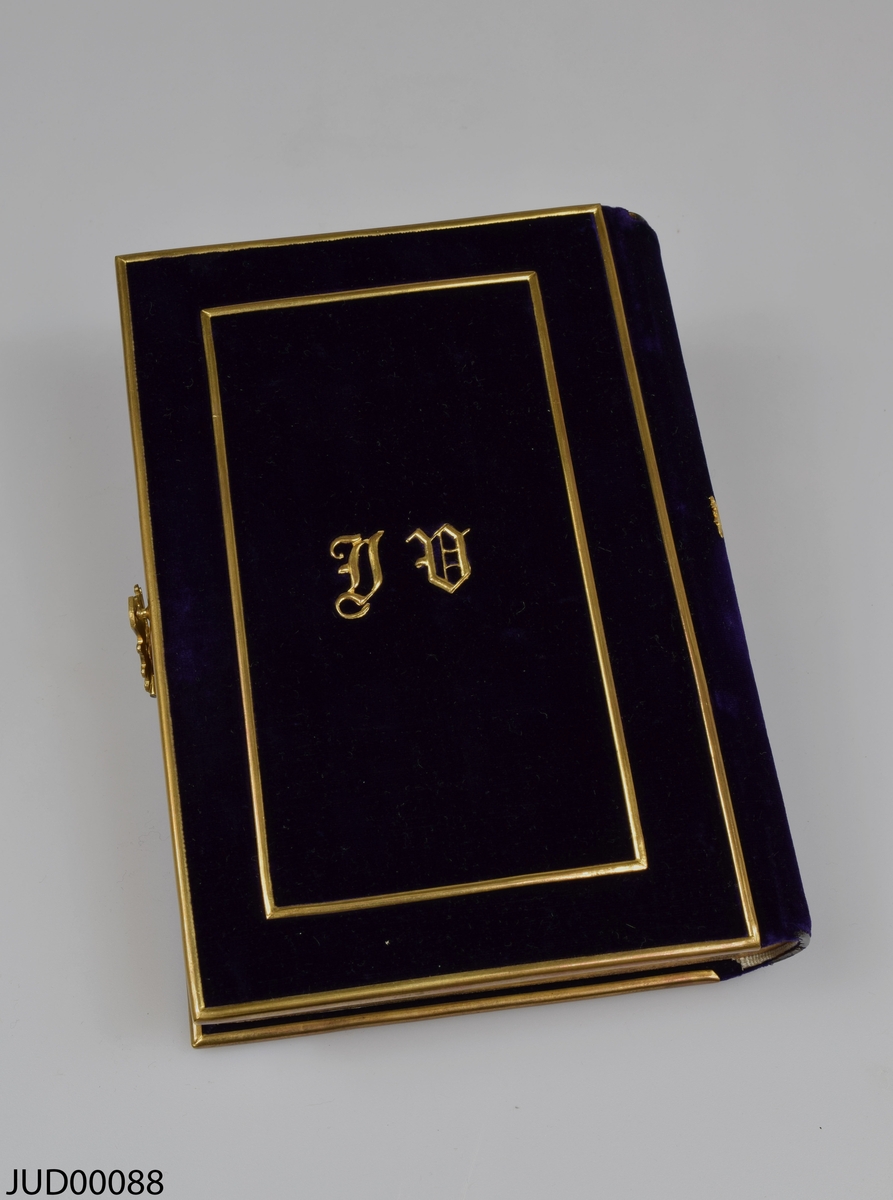 Bönbok (siddur) med sammetsomslag i djupt lila, med guldfärgat lås på sidan. Framsidan av boken dekorerad med initialerna A E i guldfärg. Boken är skriven på franska och hebreiska, och är tryckt 1869.