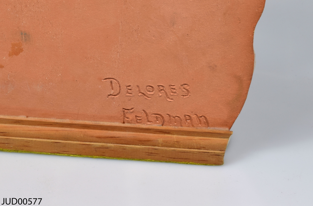 Ljusstake med nio ljushållare tillverkad av glaserat lergods i ljusrosa och ljusgrönt. Undersidan av chanukian är klädd med limegrönt filttyg. På baksidan signerad Dolores Feldman.