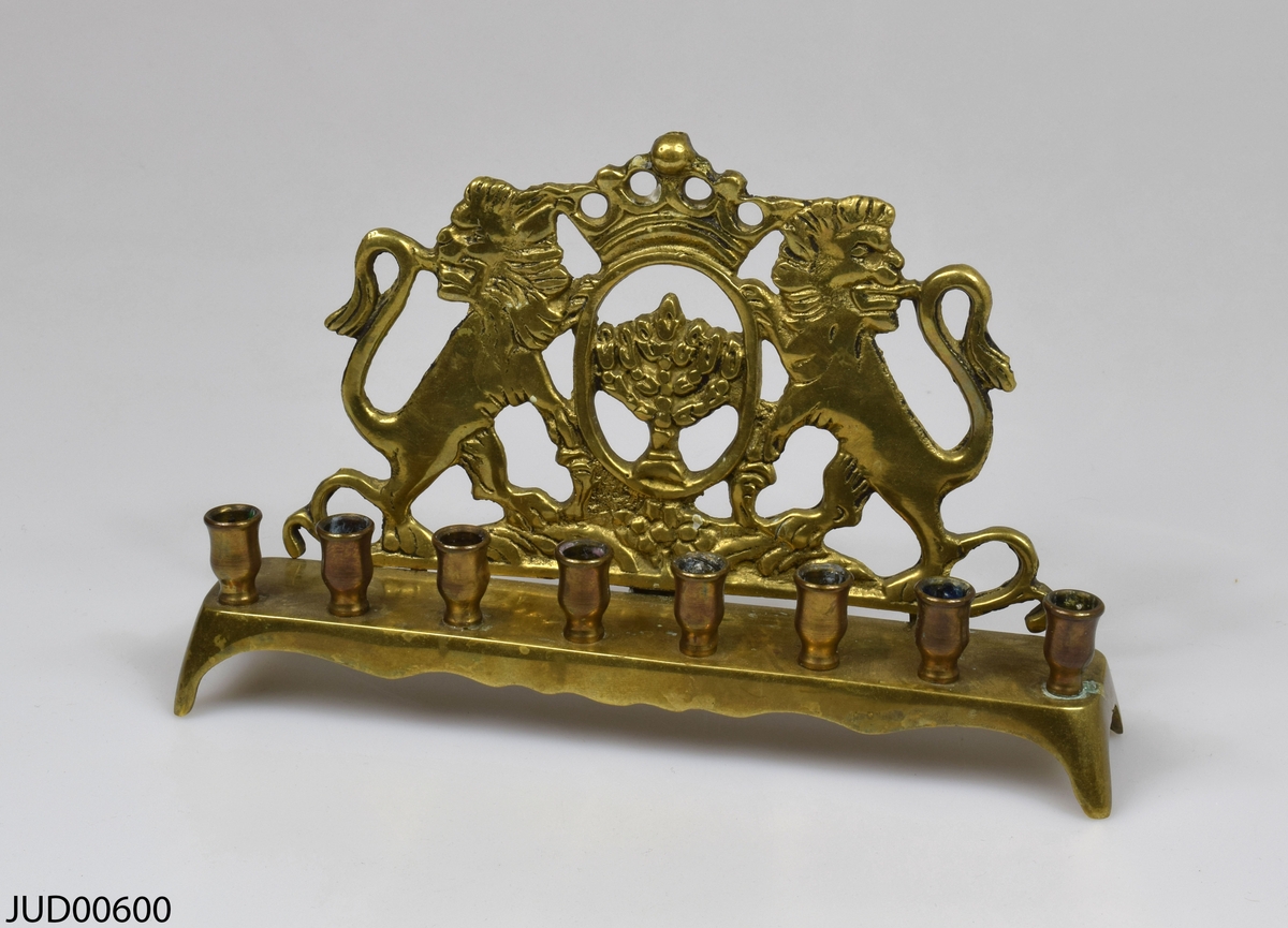 Gjuten mässingsljusstake med åtta ljushållare. Ryggen är dekorerad med menora flankerad av två lejon.