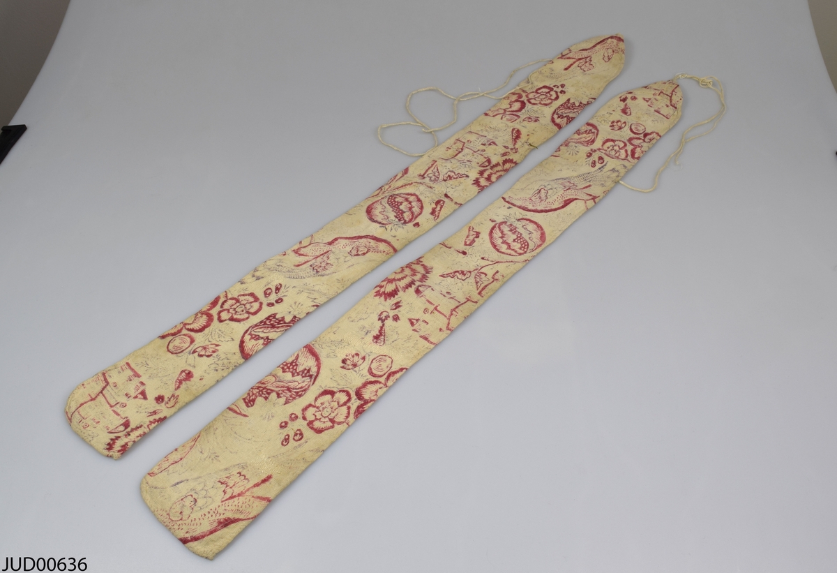 Två långa tygstycken med rött blomstermotiv på vit botten, med snöre i ena änden.