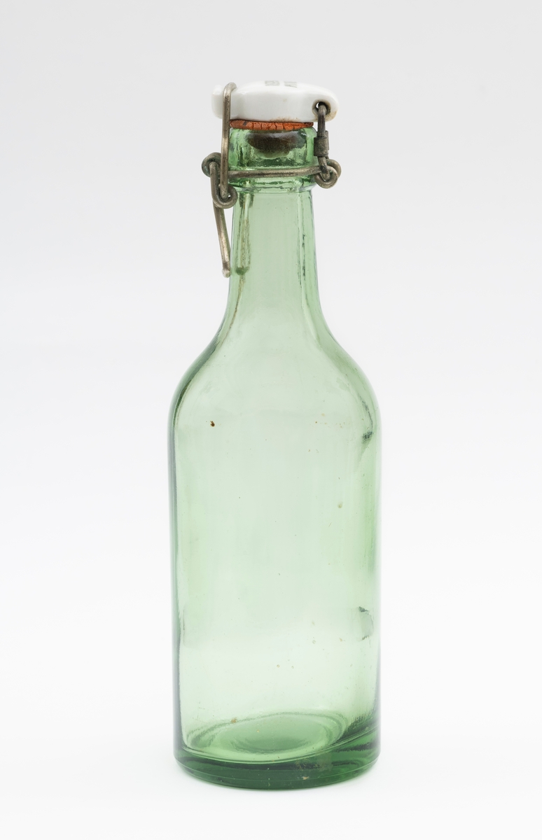 Flaske av grønt glass, antakelig opprinnelig brus- eller ølflaske, som kan ha vært gjenbrukt til aldre drikkevarer, for eksempel husholdningssaft. Flaska er 20 centimeter høy (uten kork). Den har en sylindrisk kropp med cirka 6,6 centimeters diameter. Cirka 12 centimeter fra standflata går den sylindriske delen over i ei innoverskrånende skulder mot en mer sylindrisk hals. Den midtre delen av flaskebotnen er oppoverkuvet. Flaska kan romme cirka 3 desiliter væske. Godset omkring munningen - «flasketuten» - er noe tjukkere enn i flaska for øvrig, og her er det et spor som har gitt feste for en såkalt «patentkork». Dette er en propp, utført i kvitt porselen, som er hengslet til flasketuten ved hjelp av ståltråd, som er forankret i det nevnte sporet omkring flasketuten slik at proppen faller ned i flaskemunningen og kan låses der ved hjelp av ei ståltrådspenne, som når flaska lukkes omslutter en tapp i den fremre enden av porselenselementet. Undersida av denne komponenten har vært utstyrt med en rødfarget gummipakning, som skulle skape et vakuum i flaska. Her er pakningen bare delvis intakt. Oversida av porselenselementet er merket «ELVERUM BRYGGERI» (jfr. fotografiet SJF-F.013394).