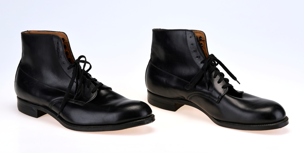 Et par høyskaftede herresko i størrelse 11 produsert av Stone-Tarlow. Skoene er sydd av svart skinn. Foran er de avrundet spiss. I front er det 10 par snørehull. Det er svarte metallmaljer på baksiden av snørehullene. Skoene er snøret med svarte, flate skolisser. Under snøringen er det en tunge av svart skinn som er foret med tynt ullfor. Innvendig er skoene foret med gråhvittt lerretsstoff. Det er innersåle av lyst brunt lær. Langs kanten oppe og kantene med snørehull er det også foret med lyst brunt skinn. På skoene er det dekor i form av stikninger. Skoene har yttersåle av brunt lær. Hælene har gummiflikk.