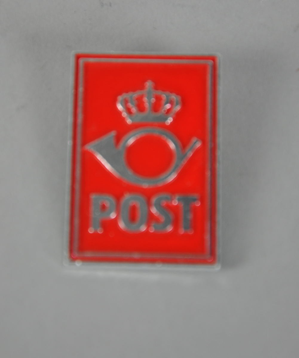 Rektangulær nål med festeanordning på bakside. Rød bunnfarge med kronet posthorn og innskriften "POST".