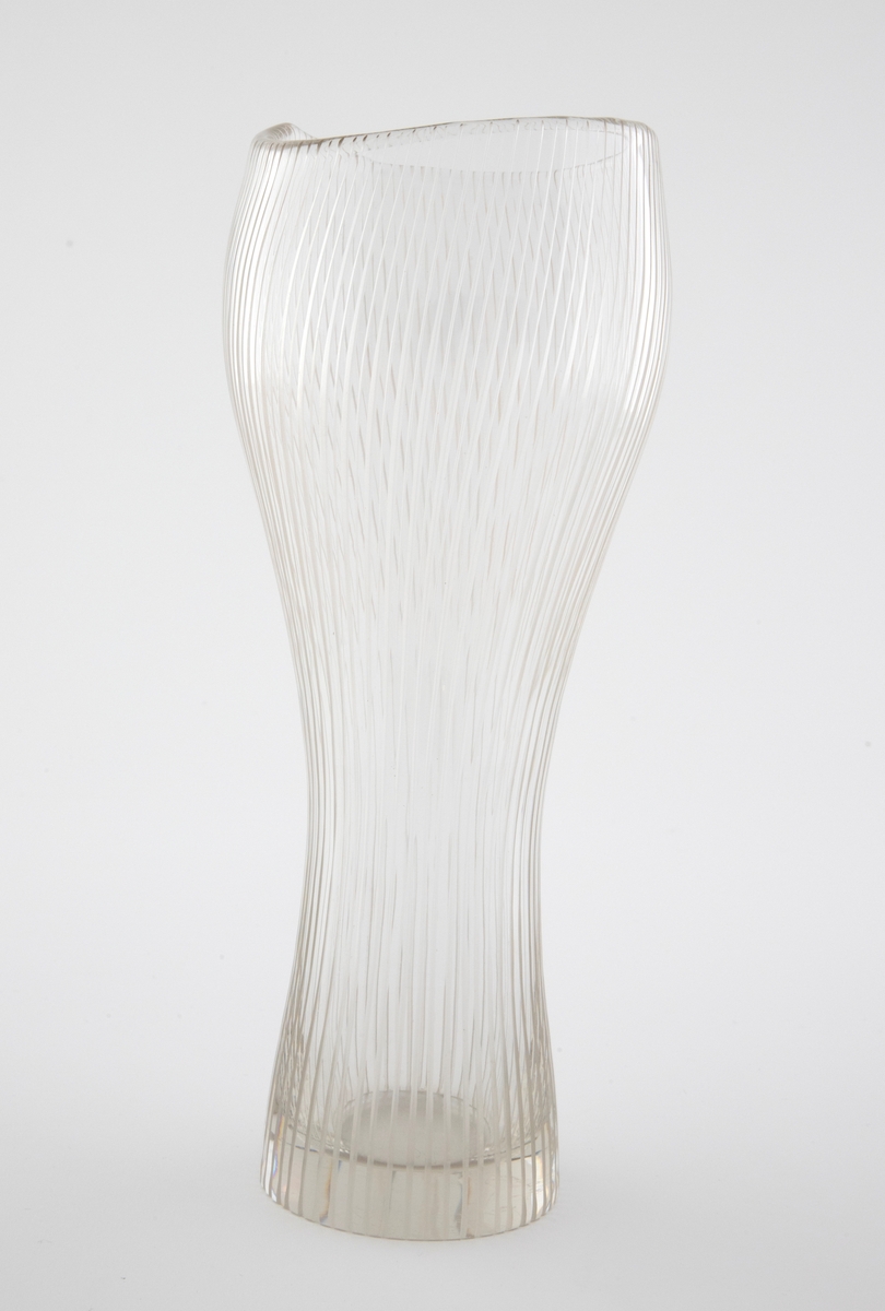 Høyreist vase i klart glass. Uregelmessig, bølgende munningskant. Korpus er dekorert med hjulgravering i form av spiralformede, vertikale linjer; dobbelt så mange linjer på over- som på underdelen.