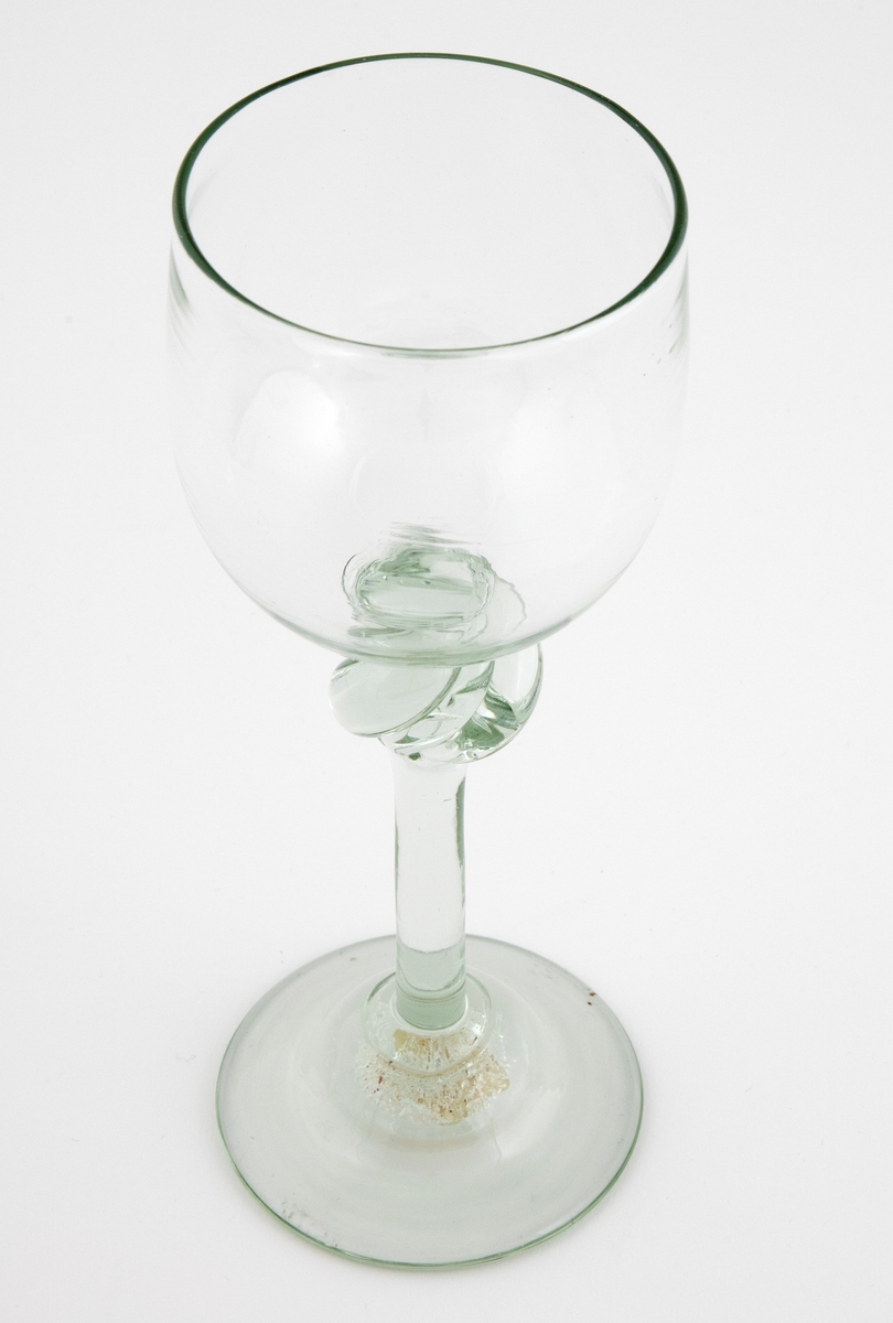 Drikkeglass i klart grønntonet glass med klokkeformet kupa, som hviler på en tynn stett med spiralformet vulst. Rund fotplate, noe opphøyet i midten.