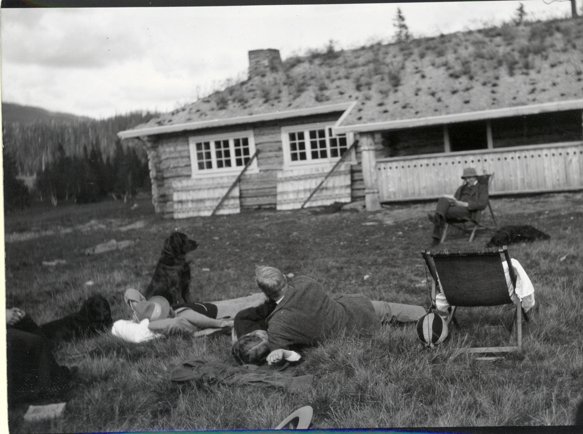 Fire medlemmer av jaktlaget, Westye Egeberg, forstmester Solberg samt Ingeborg og Nils O.Y. Fearnley hviler ut på tunet til sistnevntes jakthytte i Fjergen, Nord-Trøndelag. Fotografert en søndag 1910.