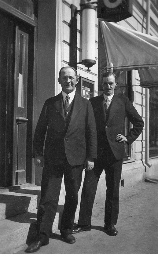 Två män i kostym står på trottoaren utanför en affär.