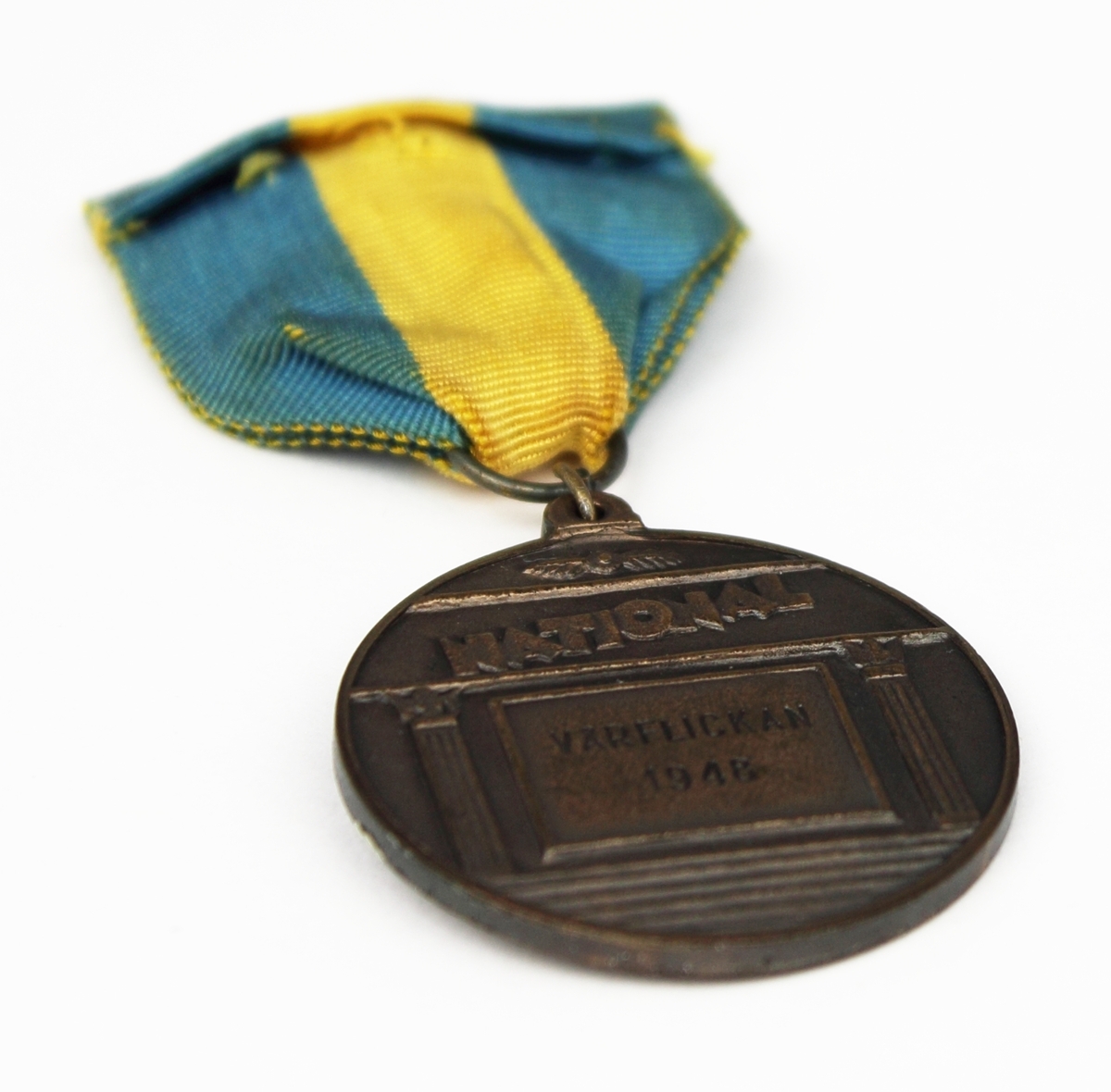 Medalj i brons fäst på blågult band. Medaljen har rund form med en naken kvinna i relief på framsidan.