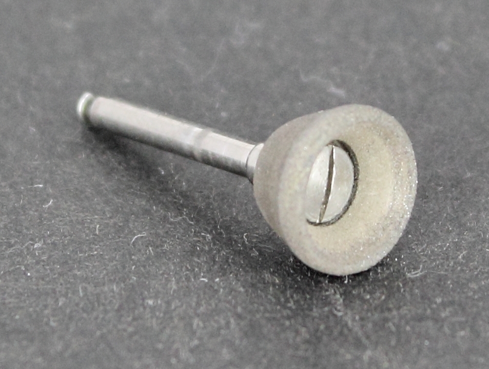 Skålformad rund gummitrissa med cylinderformat skaft för infästning i handstycke. Trissan är fäst i skaftet med en enkelspårig skruv. Något sliten efter användning, ett litet hack finns i kanten.