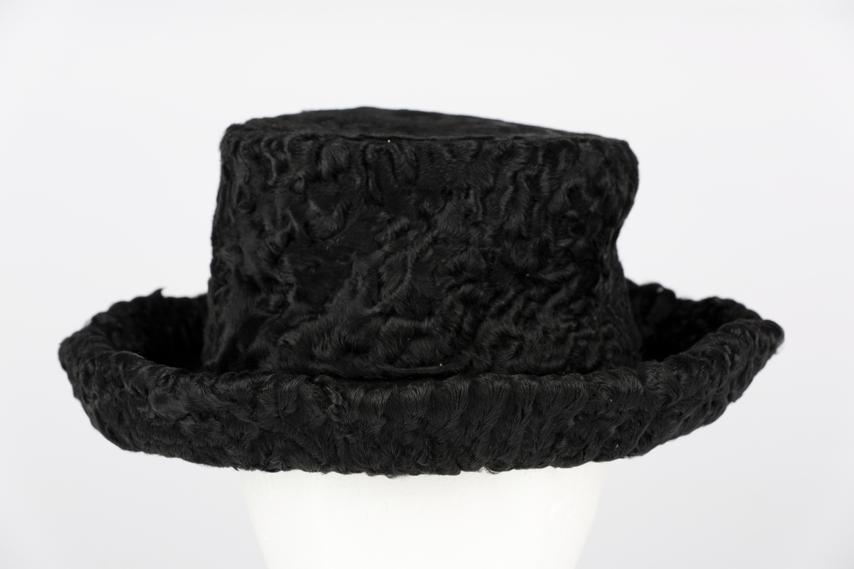 Hattepull i persianerskinn. Bremi sort filt trukket på undersiden med sort persianerskinn. Pyntesløyfe i skinn.